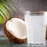 Glass with fresh coconut water and coconuts on the table.