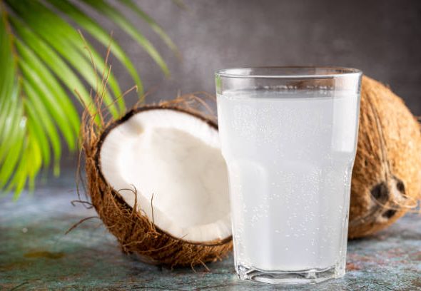 Glass with fresh coconut water and coconuts on the table.
