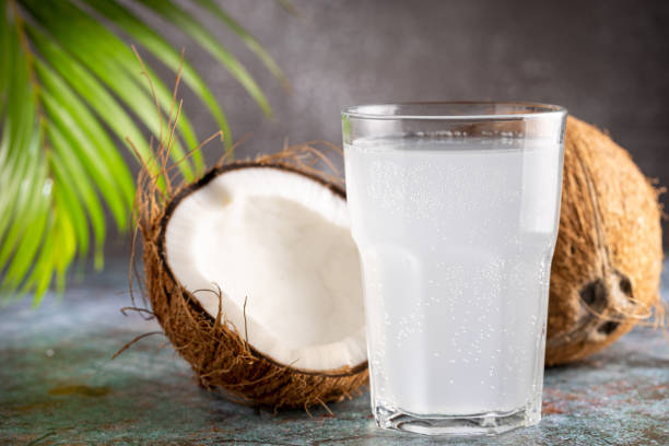 Glass with fresh coconut water and coconuts on the table.